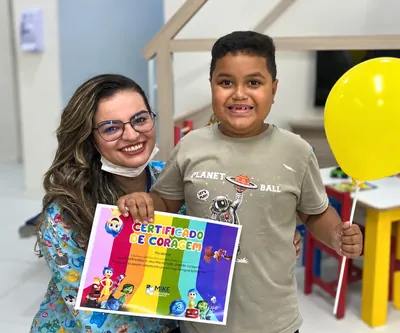 Profissional de óculos e paciente com certificado colorido e balão amarelo.
