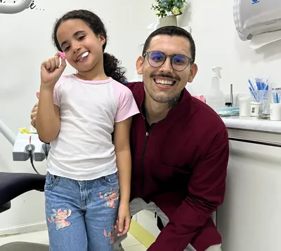 Menina de camiseta branca ao lado de um profissional de óculos.
