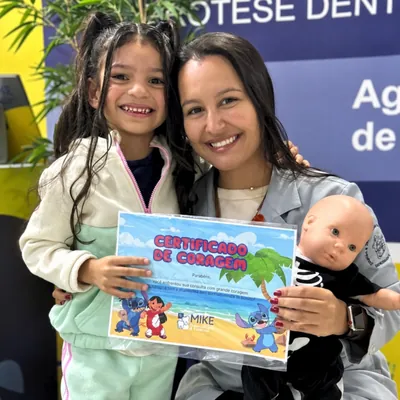 Menina com certificado azul, profissional e boneca na clínica.