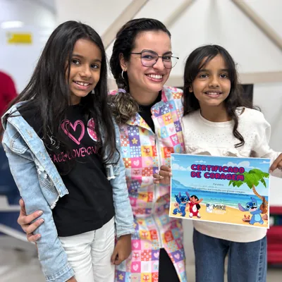 Profissional de óculos entre duas meninas com certificado colorido.