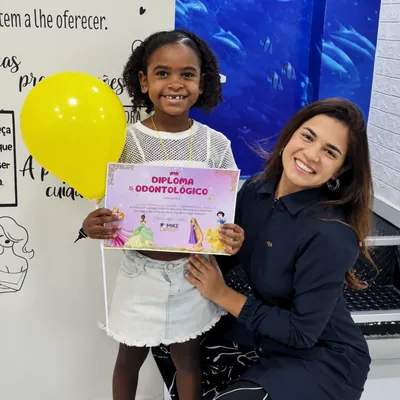 Menina com diploma e balão amarelo ao lado de uma profissional.