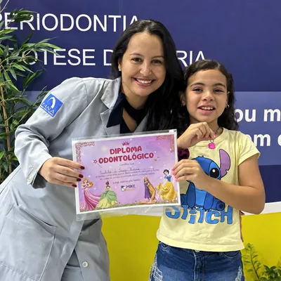Menina com certificado rosa ao lado de uma profissional.