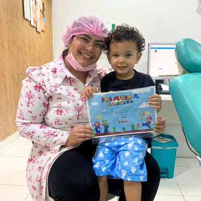Menino com certificado azul ao lado de uma profissional de touca rosa.