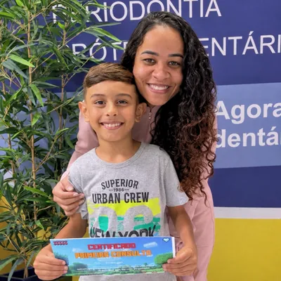 Menino com certificado ao lado de uma mulher de cabelo cacheado.